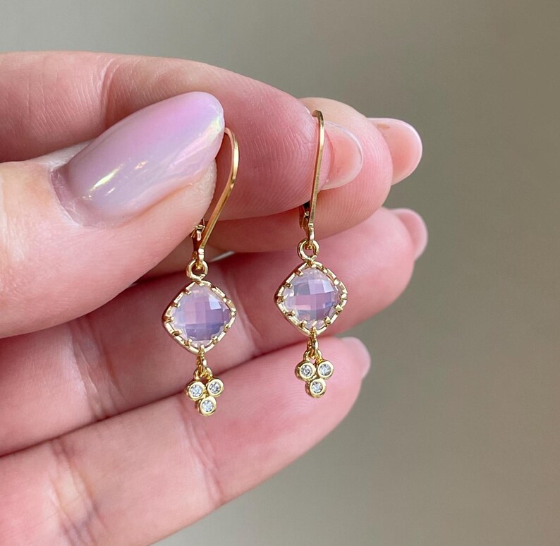 May include: A pair of gold earrings with a light pink square gemstone and a cluster of smaller clear gemstones dangling below.