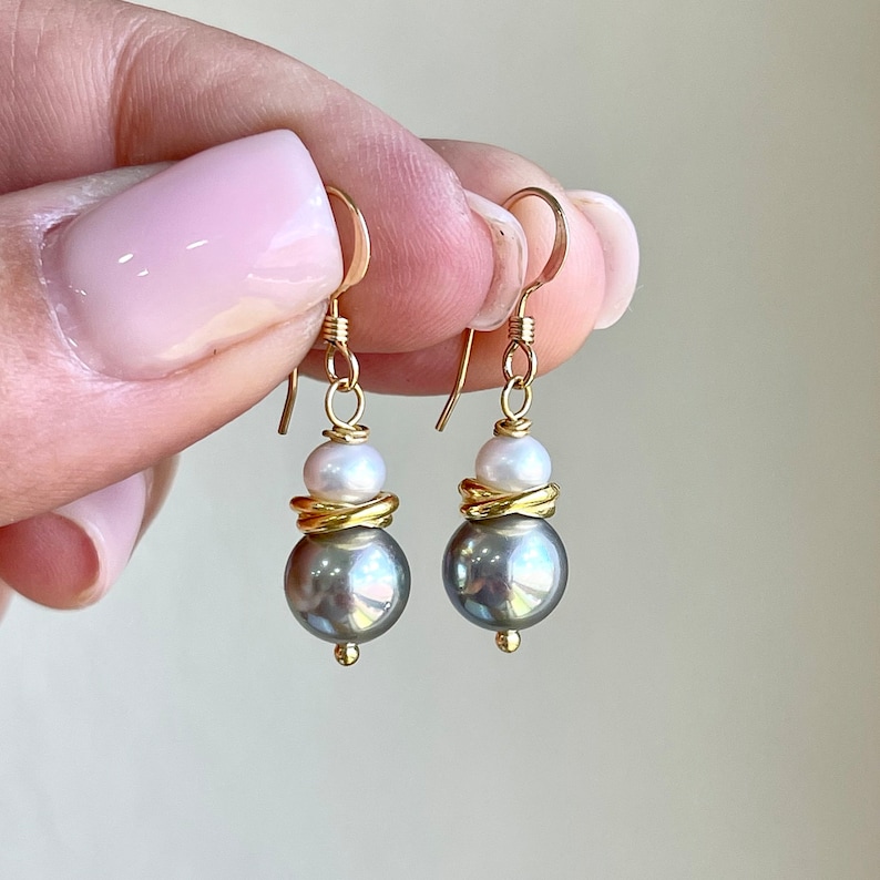 May include: Gold-tone drop earrings featuring a gray pearl base, a white pearl accent, and a gold-tone spiral detail. The earrings have a simple hook closure. These elegant earrings are a perfect accessory for any occasion.