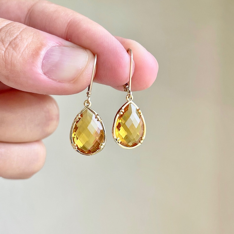 May include: A pair of gold teardrop earrings with faceted amber-colored stones.