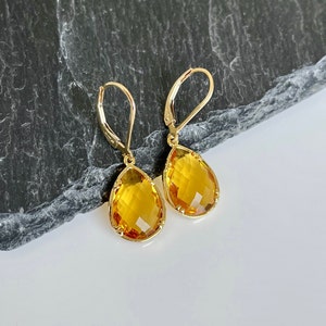 May include: A pair of gold teardrop earrings with yellow topaz gemstones.