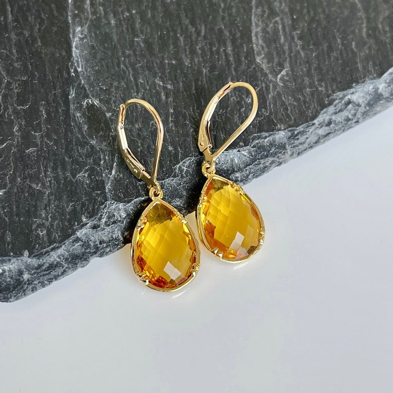 May include: A pair of gold teardrop earrings with yellow topaz gemstones.