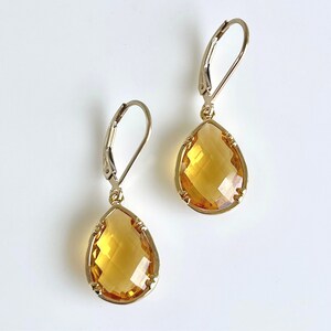 May include: A pair of gold teardrop earrings with faceted amber-colored stones. The earrings have a leverback closure.