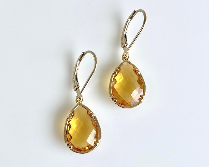 May include: A pair of gold teardrop earrings with faceted amber-colored stones. The earrings have a leverback closure.