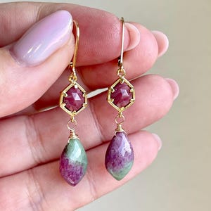 Peut inclure: Boucles d'oreilles en or avec des pierres précieuses roses et vertes. La pierre précieuse supérieure est de forme carrée facetée et la pierre précieuse inférieure est de forme larme.