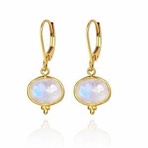 May include: A pair of gold-colored leverback earrings. Each earring features an oval, iridescent, white gemstone set in a gold bezel. A small, decorative gold element is below the gemstone.