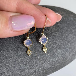 May include: A pair of gold earrings with a light pink square gemstone and a cluster of small clear gemstones dangling below.