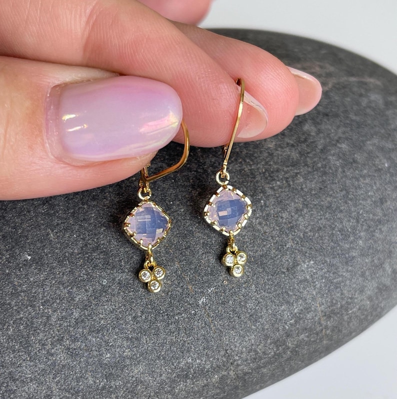 May include: A pair of gold earrings with a light pink square gemstone and a cluster of small clear gemstones dangling below.