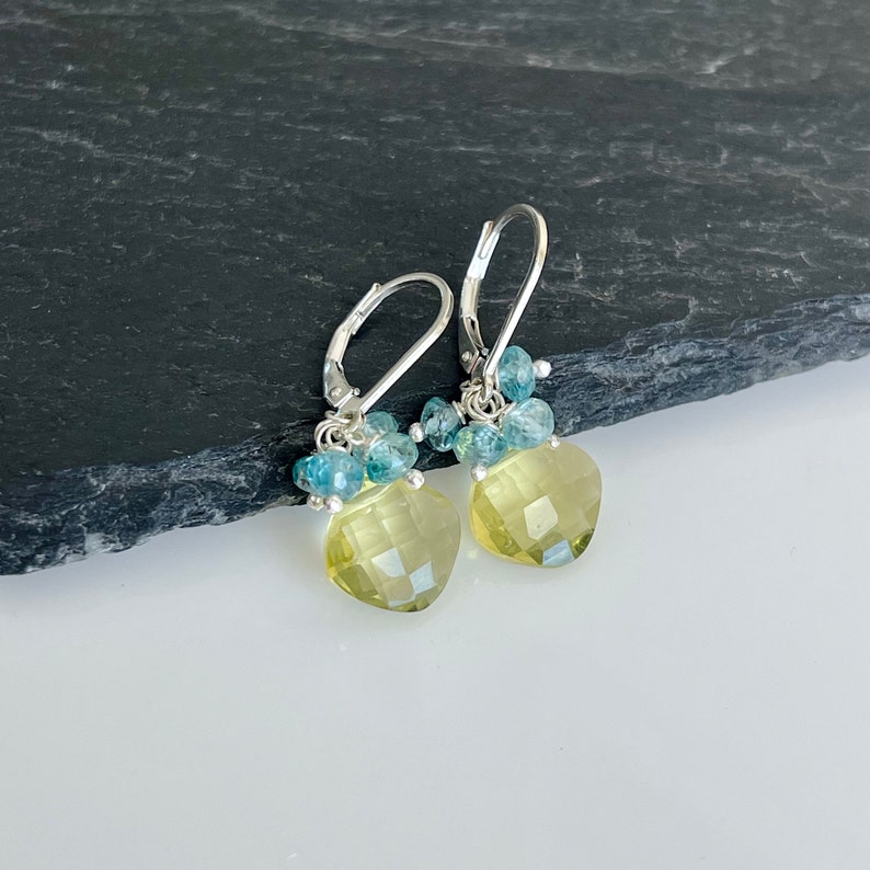May include: A pair of silver earrings with a yellow heart-shaped gemstone and blue gemstone accents.