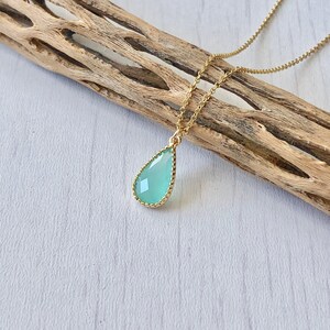 Puede incluir: Un delicado collar de cadena dorada con un colgante en forma de l&aacute;grima que presenta una piedra preciosa verde claro. La piedra preciosa est&aacute; rodeada por un borde dorado.