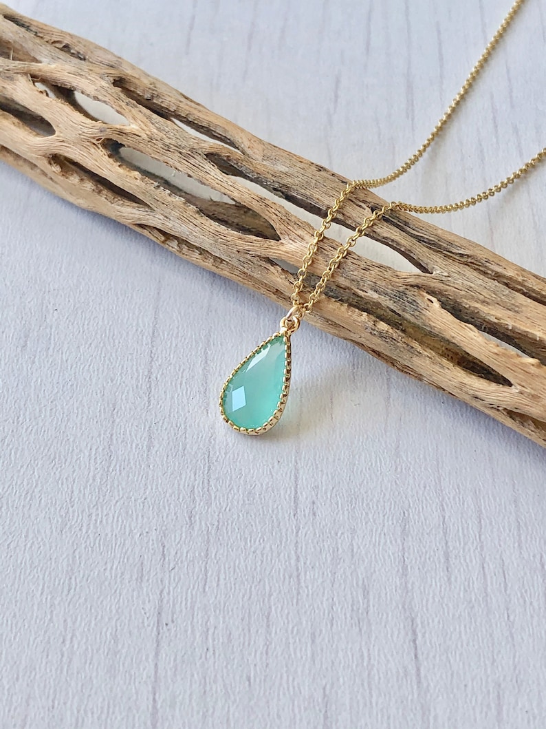 Puede incluir: Un delicado collar de cadena dorada con un colgante en forma de l&aacute;grima que presenta una piedra preciosa verde claro. La piedra preciosa est&aacute; rodeada por un borde dorado.