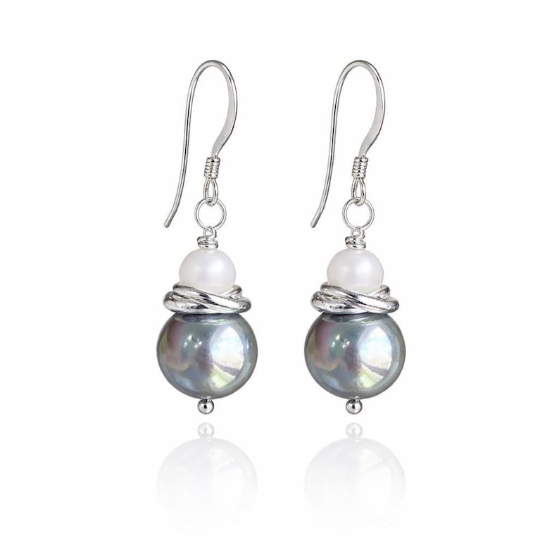 May include: A pair of dangle earrings featuring a large, iridescent gray pearl, a smaller white pearl, and silver-toned metal accents. The earrings have a hook closure and a reflective surface.