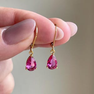 May include: A pair of gold dangle earrings with pink pear-shaped gemstones.