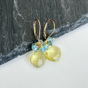 May include: Gold earrings with a teardrop shaped yellow citrine gemstone and blue topaz accents.