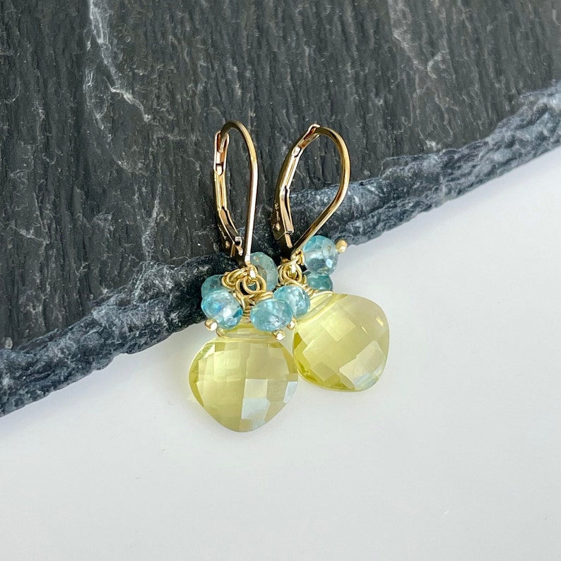 May include: Gold earrings with a teardrop shaped yellow citrine gemstone and blue topaz accents.