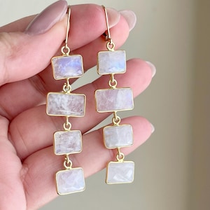 May include: Gold dangle earrings with four rectangular moonstone stones.