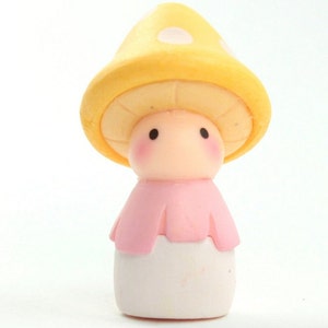 May include: A small, yellow mushroom-shaped figurine with white polka dots. The figurine has a pink dress and a white base.