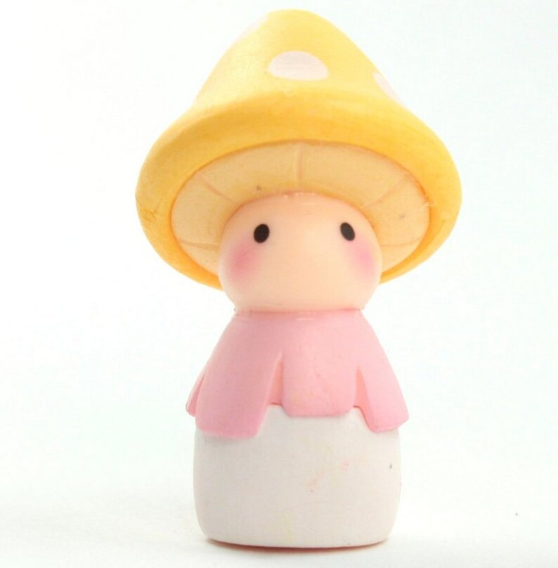 May include: A small, yellow mushroom-shaped figurine with white polka dots. The figurine has a pink dress and a white base.