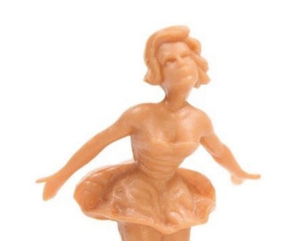 May include: A tan plastic figurine of a ballerina wearing a tutu. The figurine is posed with one arm raised and the other arm extended to the side.