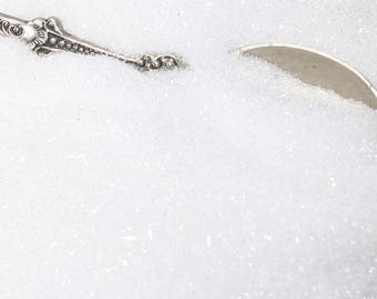May include: A close-up of a white glitter, resembling snow, with a silver spoon partially submerged in it.