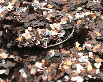 May include: Close-up of a pile of copper and brown glitter flakes. The glitter is iridescent and has a metallic sheen.