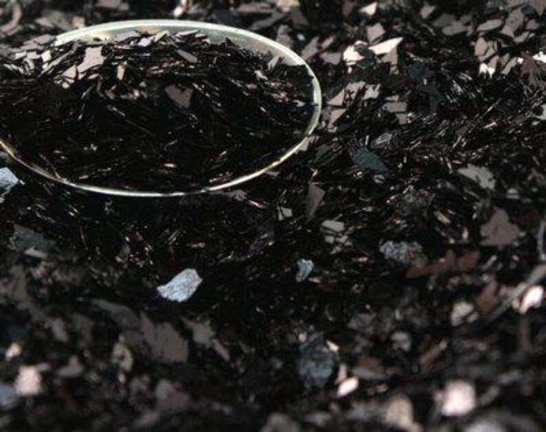 May include: A close-up of black glitter, a popular material for crafting and decorating. The glitter is in a small spoon, showing its texture and sparkle.