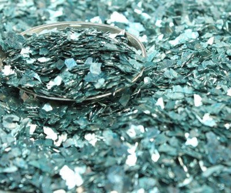 May include: A close-up of teal blue iridescent glitter, perfect for crafting and adding sparkle to projects.