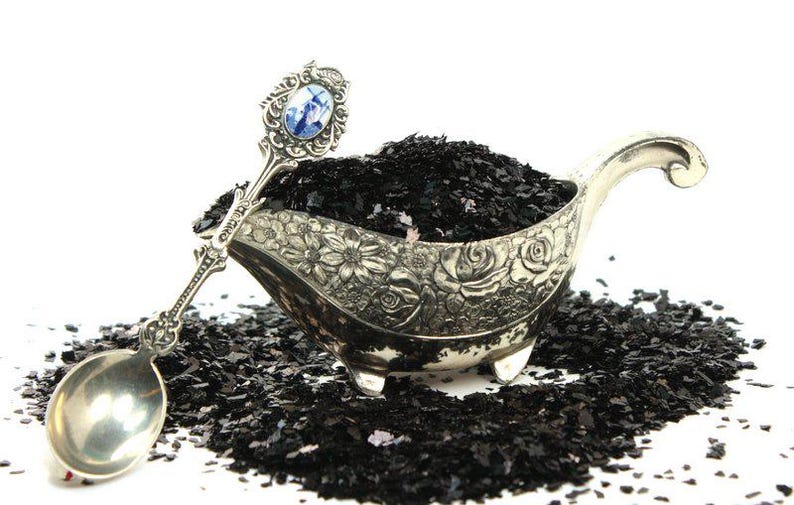 May include: A silver serving dish with an ornate floral design, filled with black flakes. A silver spoon with a blue and white porcelain handle rests on the edge of the dish.