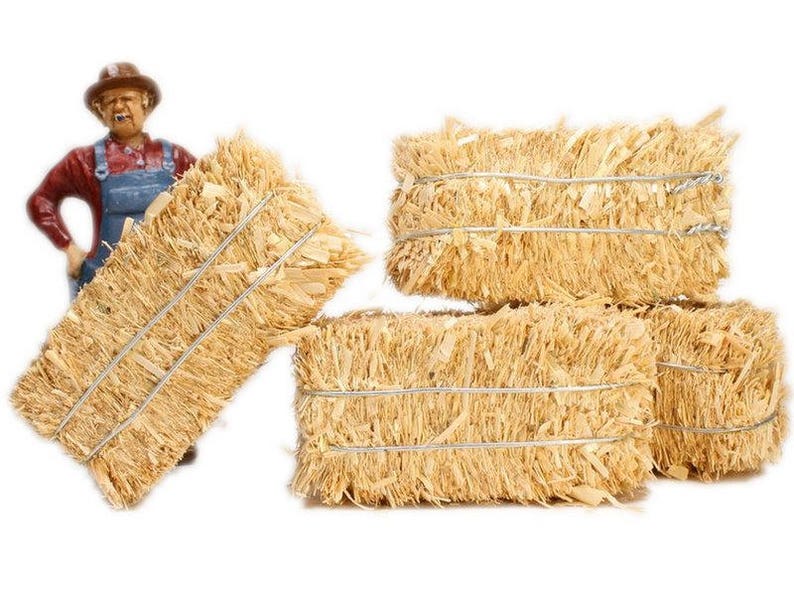 May include: Four bales of straw tied with twine, stacked on top of each other. The straw is a light brown color and has a rough texture.