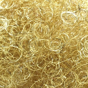 Puede incluir: Primer plano de un montón de oropel metálico dorado. El oropel está hecho de hilos finos y brillantes que están retorcidos y enroscados en una variedad de formas.