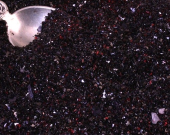 May include: A close-up of a pile of black and red glitter. A silver spoon is partially visible in the top left corner of the image.