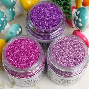 Może przedstawiać: Trzy szklane słoiki wypełnione różnymi kolorami brokatu. Słoiki są oznaczone etykietą "Glitter German Glass Meyer-Jamin".