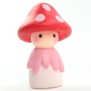 May include: A small, pink and white figurine of a mushroom person with a red and white polka dot hat.