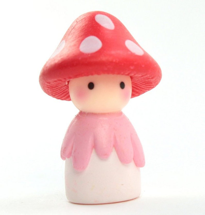 May include: A small, pink and white figurine of a mushroom person with a red and white polka dot hat.