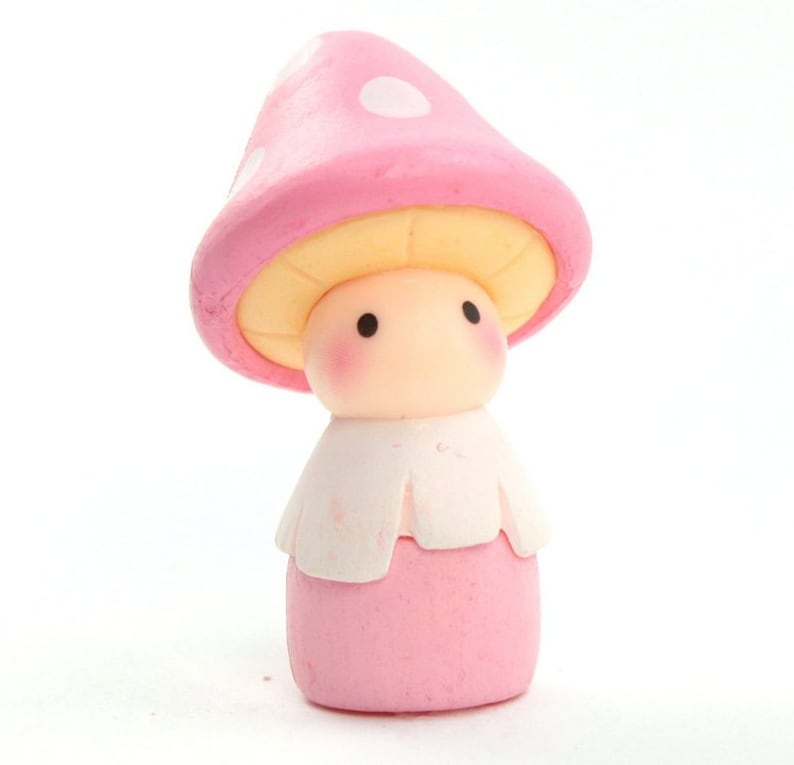 May include: A pink mushroom figurine with a white collar and a cute face. The mushroom has white polka dots on the top.