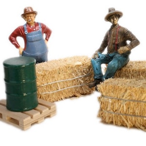 May include: Two miniature figurines of farmers, one wearing a straw hat and overalls, the other wearing a straw hat and blue jeans, sitting on bales of hay. A green barrel sits on a wooden pallet.