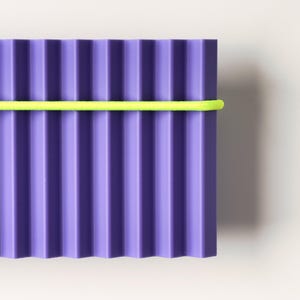 May include: A rectangular, corrugated purple object with a bright yellow band wrapped around it. The object has vertical ridges and a smooth, solid color. The background is a plain white.