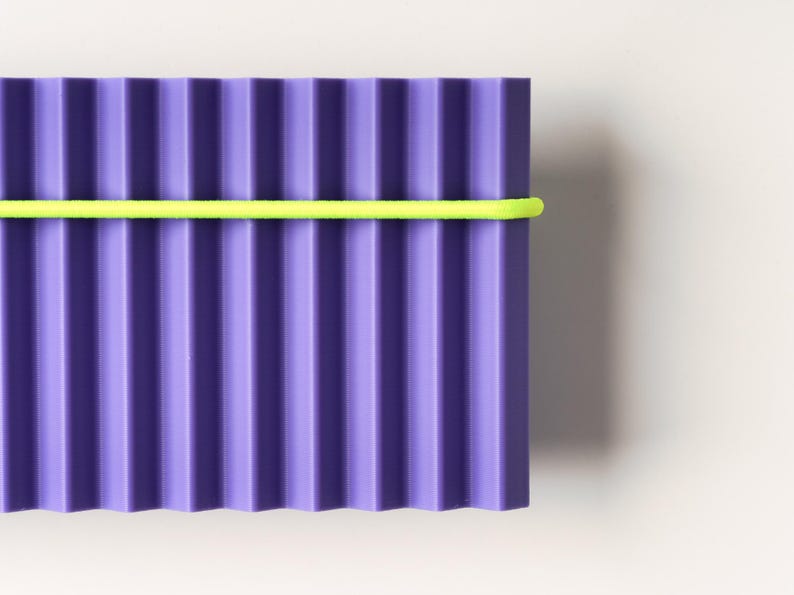 May include: A rectangular, corrugated purple object with a bright yellow band wrapped around it. The object has vertical ridges and a smooth, solid color. The background is a plain white.