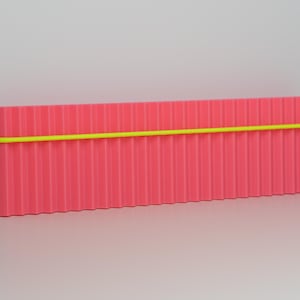 May include: A rectangular, pink container with vertical ridges and a neon yellow band wrapped around it. The container is set against a white background, creating a minimalist aesthetic. The object appears to be a storage box or organizer.