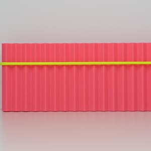 May include: A rectangular, corrugated, pink object with a bright yellow horizontal stripe. The object is set against a white background. The design is minimalist and modern.