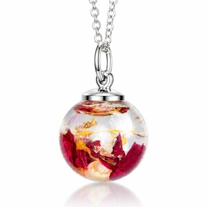 May include: A clear, spherical pendant necklace with a silver chain. The pendant is filled with red and gold floral elements. The necklace is a delicate piece of jewelry, perfect for adding a touch of nature-inspired elegance to any outfit.