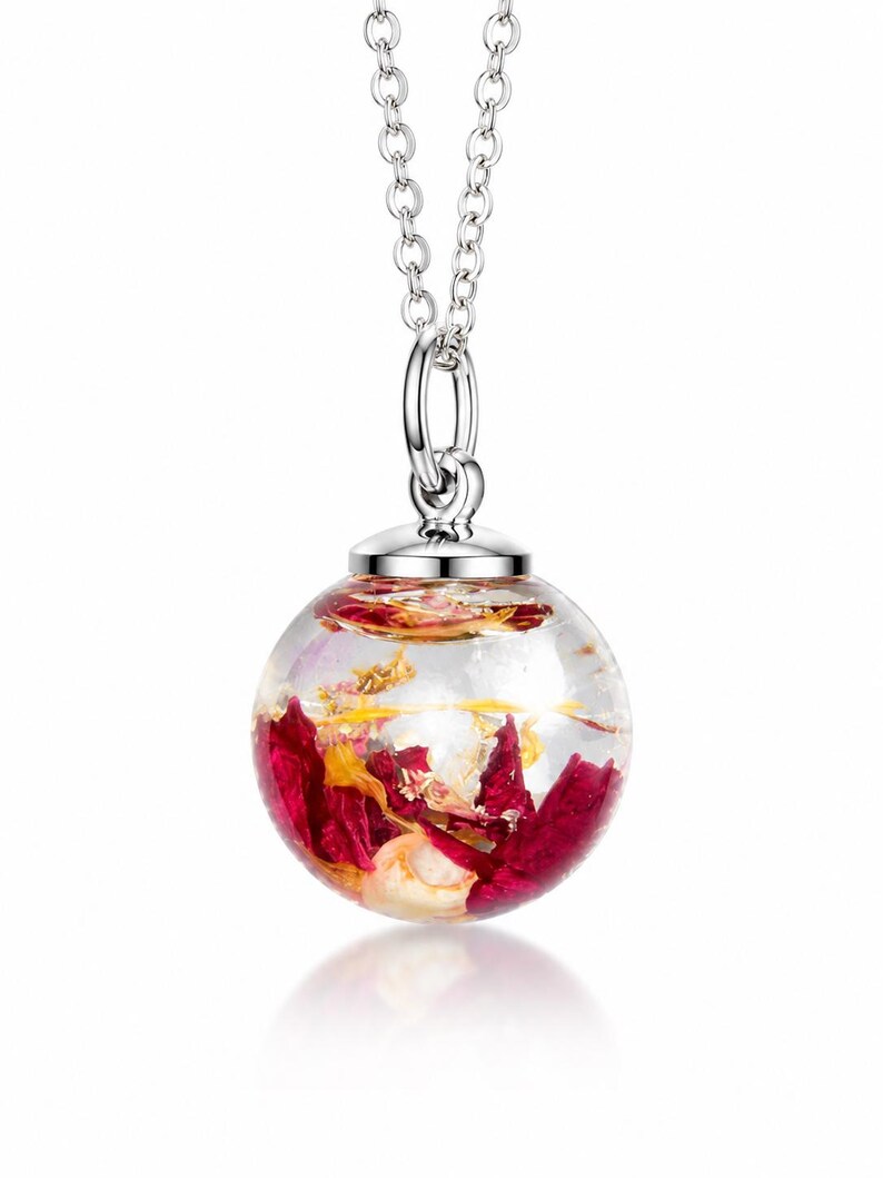 May include: A clear, spherical pendant necklace with a silver chain. The pendant is filled with red and gold floral elements. The necklace is a delicate piece of jewelry, perfect for adding a touch of nature-inspired elegance to any outfit.