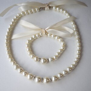 Peut inclure: Un ensemble de bijoux en perles d'ivoire avec un collier et un bracelet. Les deux pi&egrave;ces pr&eacute;sentent un seul accent en strass sur chaque perle.