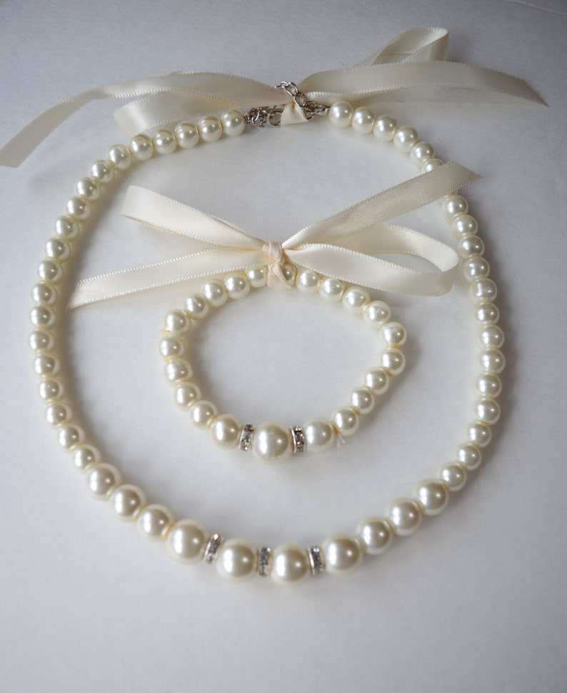 Peut inclure: Un ensemble de bijoux en perles d'ivoire avec un collier et un bracelet. Les deux pi&egrave;ces pr&eacute;sentent un seul accent en strass sur chaque perle.