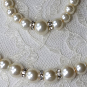 Peut inclure: Deux colliers de perles avec des accents de strass sur un fond de dentelle blanche.