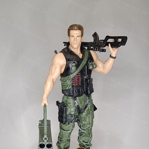 Könnte beinhalten: Eine grün-schwarze Actionfigur eines Soldaten, der eine Waffe und einen Raketenwerfer hält. Die Figur steht auf einem felsigen Sockel mit einem schwarzen runden Sockel. Der Sockel trägt die Aufschrift "COMMANDO" und "DCROW-ARTWORKS.DE".