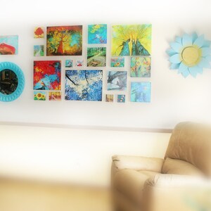 May include: A gallery wall with a variety of colorful framed artwork, including landscapes, nature scenes, and abstract designs. A blue and white paper flower decorates the wall.