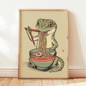 May include: Framed print of a cartoon gecko eating ramen. The gecko is green and brown, using chopsticks to eat noodles from a blue and red bowl. The artwork has a vintage style, with a light beige background.