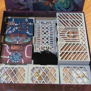 May include: Open board game box with game components. Includes game boards, white card holders with geometric cutouts, and game cards. The box is purple with a fantasy illustration on the lid.