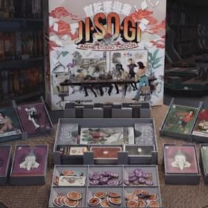 May include: A board game titled JI-SO-GI Anime Studio Tycoon featuring a large box with an illustrated office scene. The set includes multiple gray plastic card holders, stacks of illustrated game cards, and a tray filled with circular tokens.