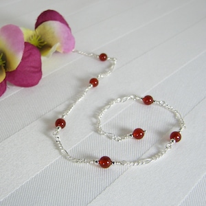 May include: A silver chain necklace and bracelet set with red carnelian beads. The necklace is longer than the bracelet.